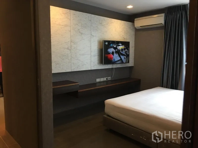 Condominium for rent in Watthana, Bangkok - Bedroom with queen bed, wall-mounted TV, built-in shelf, air conditioner and blackout curtains.