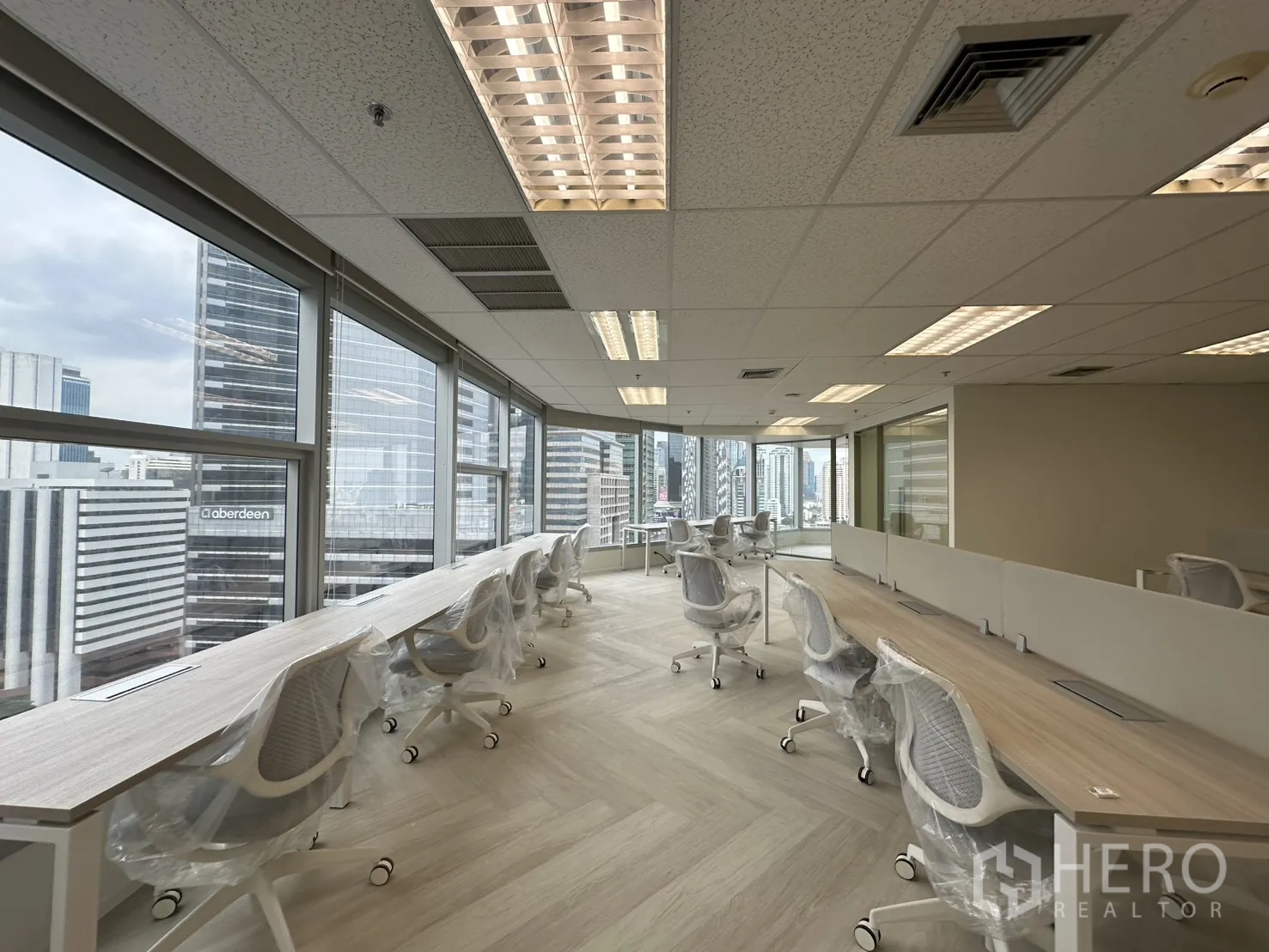 ออฟฟิศ for rent in Sathon, Bangkok - โต๊ะทำงานยาวริมหน้าต่างพร้อมวิวเส้นขอบฟ้าและไฟฟลูออเรสเซนต์เหนือศีรษะ