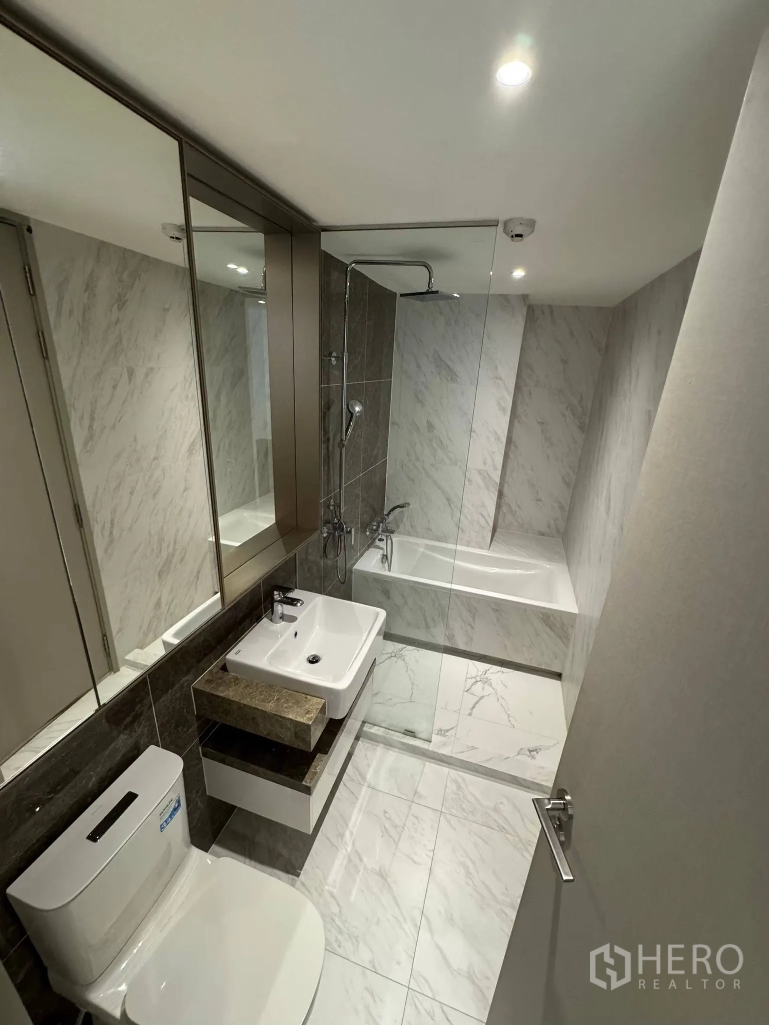 Condominium for rent in Khlong Toei, Bangkok - Modern bathroom with rain shower over bathtub, vanity and full-height mirrors.