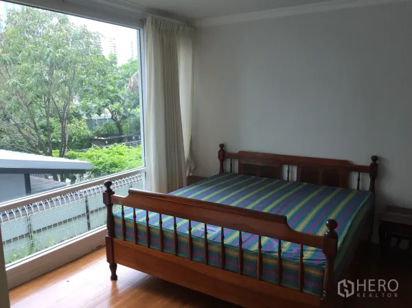 Condominium for sale in Khlong Toei, Bangkok - Bedroom with wooden bed frame and floor-to-ceiling window overlooking greenery.