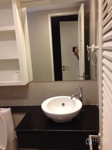 Condominium for rent in Khlong Toei, Bangkok - Bathroom vanity with round vessel sink, large mirror and white storage cabinets.