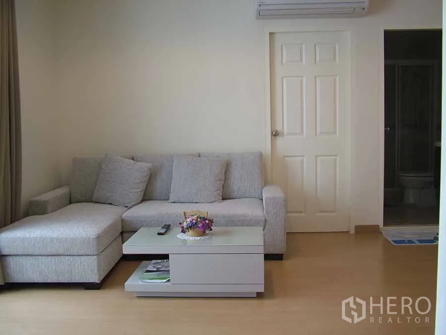 Condominium for rent or sale in Watthana, Bangkok - Bright living room of a 2-bedroom condo in Watthana, Bangkok with a gray L-shaped sofa, coffee table and wall-mounted air conditioner.