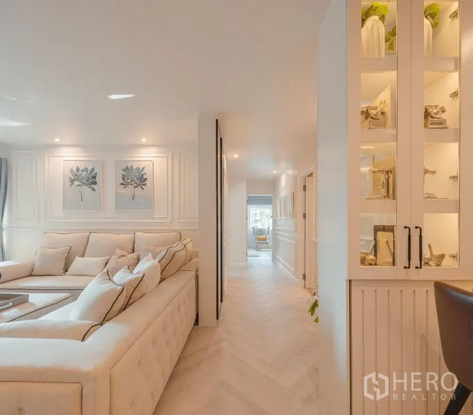 Condominium for sale in Yan Nawa, Bangkok - Spacious lounge with tufted sofa, botanical wall art, and corridor to private rooms.