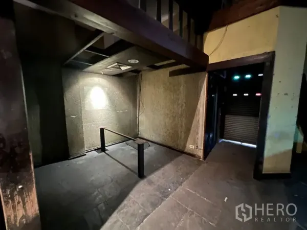 店屋 出售在Bang Rak, Bangkok - 一层昏暗空间，水泥地面，夹层梁与卷闸入口。