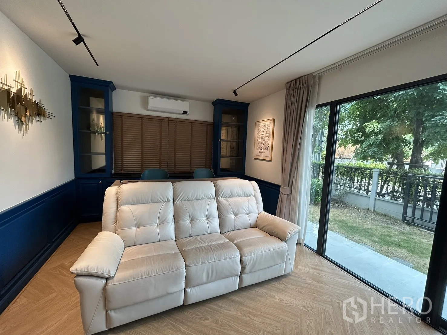 Detached House for rent in Bang Phli, Samut Prakan - Living room with sofa, blue built-ins, and garden outlook through glass.