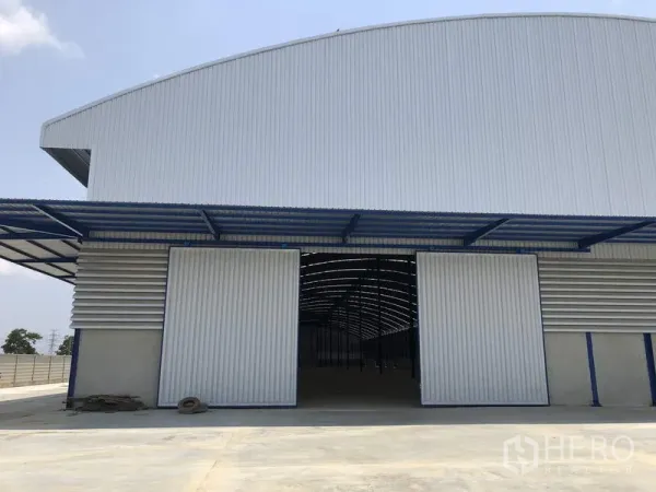 Factory for rent or sale in Lat Lum Kaeo, Pathum Thani - Front facade with large sliding doors partially open, revealing the high-clear interior.