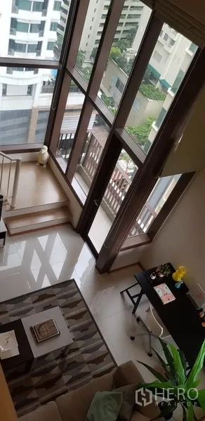 公寓 出租在Khlong Toei, Bangkok - 挑高落地窗的客厅，可观城市景色并通往阳台。