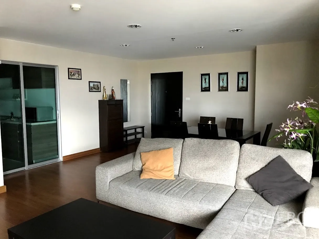 Condominium for rent in Huai Khwang, Bangkok - Spacious living and dining area with gray sectional sofa, dining table and sliding kitchen door.