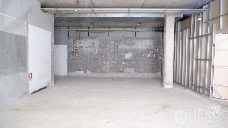 零售空间 出租在Watthana, Bangkok - 宽阔店面，结构柱与外露管线，混凝土墙面待翻新。