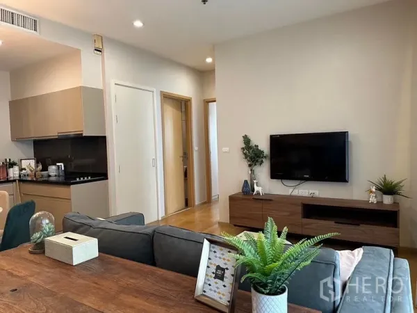 Condominium for rent in Watthana, Bangkok - Open-plan living room with wall-mounted TV, wooden console and grey sofa beside the kitchen.