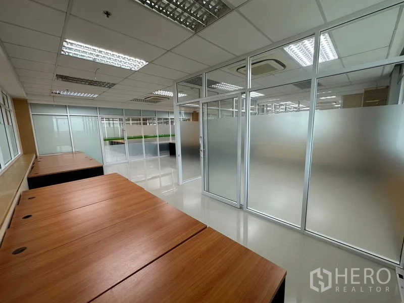Office Space for rent in Suan Luang, Bangkok - Row of wooden desks beside glass partitions inside a modern, well-lit office workspace.