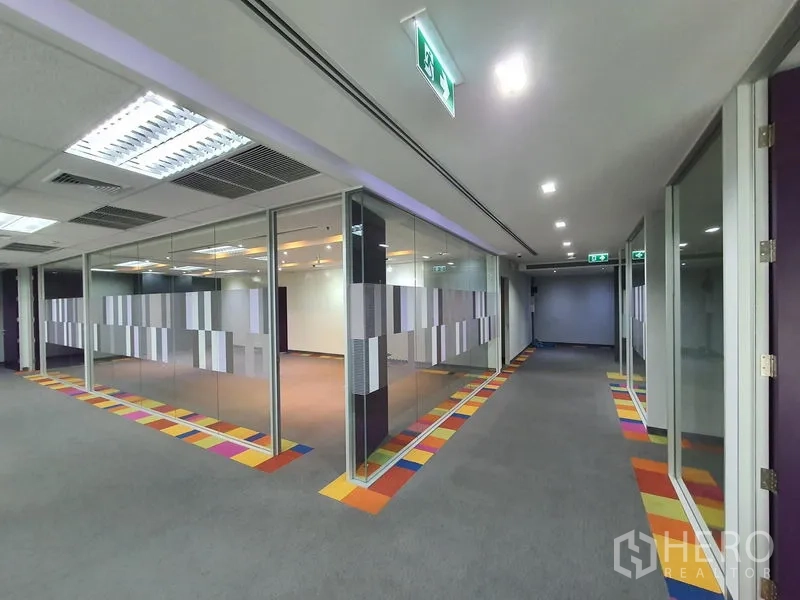 Office Space for rent in Watthana, Bangkok - Corridor with multiple glass offices, exit signs, and ceiling lights.