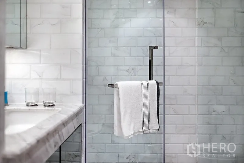 公寓 出租在Bang Rak, Bangkok - 现代浴室，石材台面与玻璃淋浴间，白色地铁砖墙面。