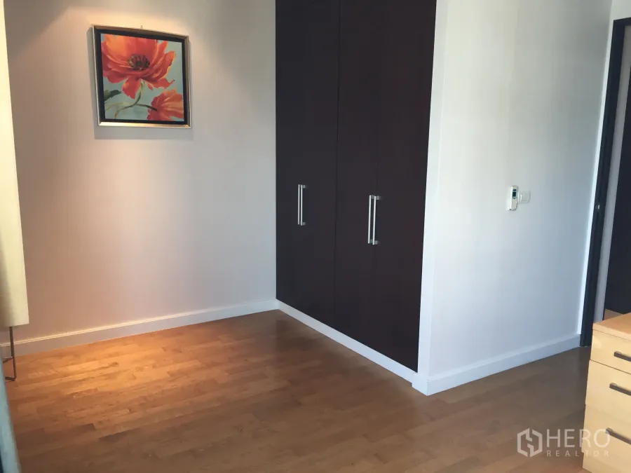 คอนโด ให้เช่าในWatthana, Bangkok - มุมห้องนอนพร้อมตู้เสื้อผ้าบิลต์อินสีเข้ม พื้นไม้ และภาพวาดดอกไม้ ในคอนโดโซนพร้อมพงษ์