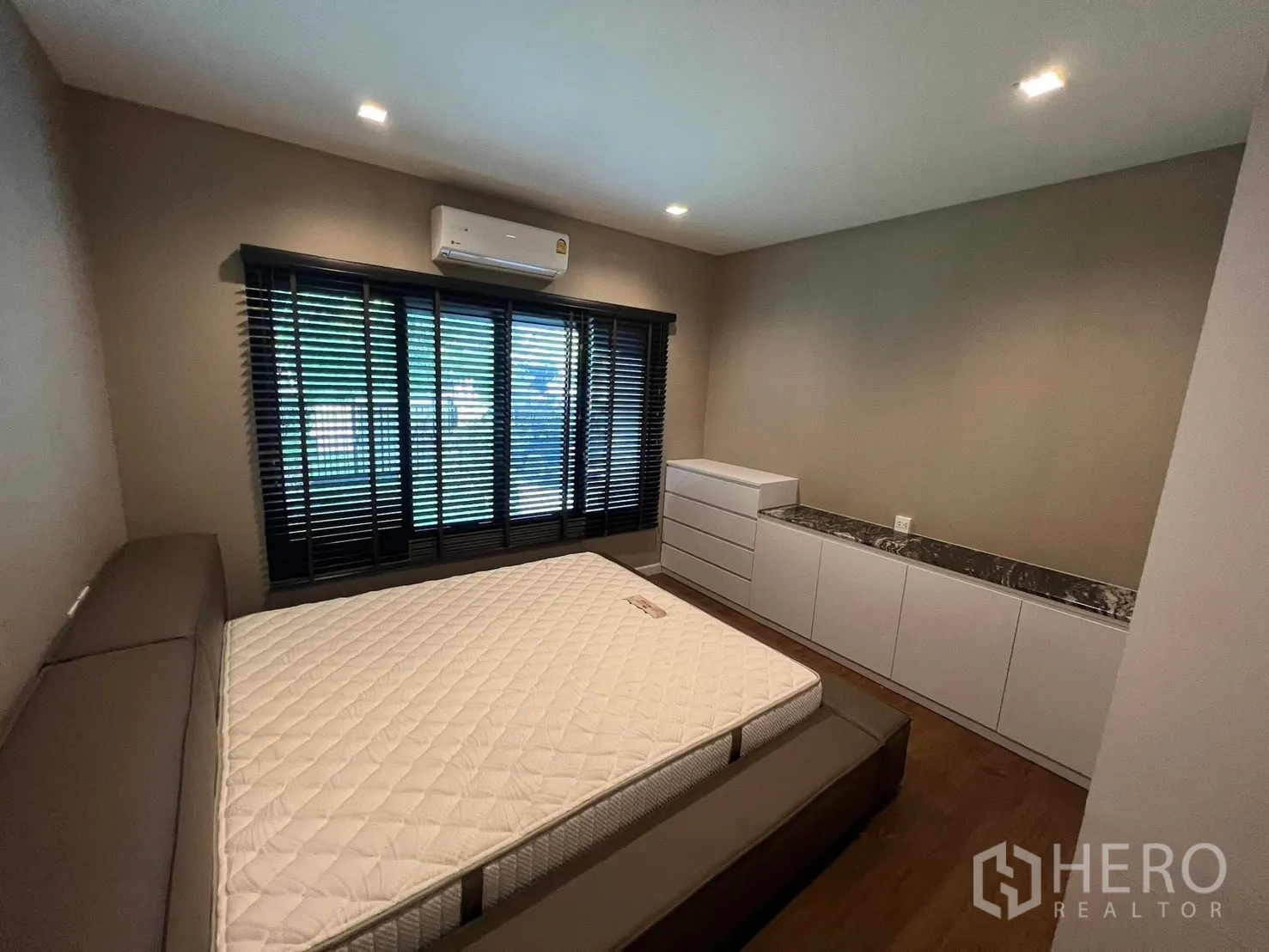 Detached House for rent in Bang Phli, Samut Prakan - Bedroom with long low storage cabinets topped in marble, dark blinds, and a platform bed.