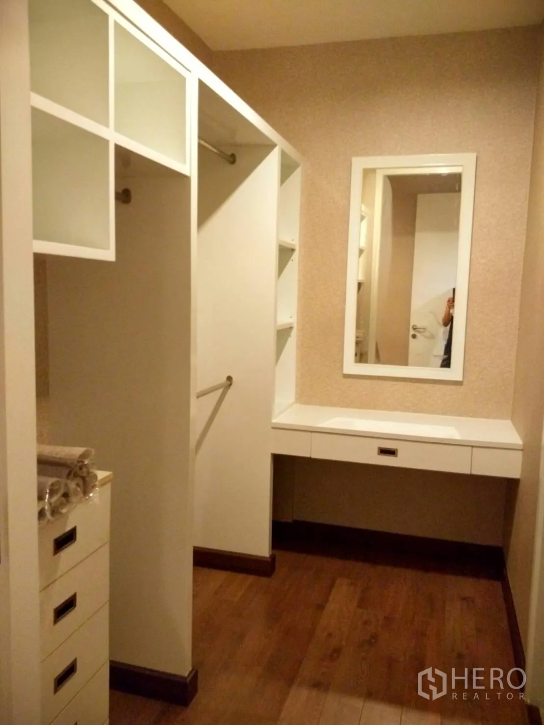 Condominium for rent in Phra Khanong, Bangkok - Walk-in closet featuring built-in white wardrobes, drawers, and a dressing vanity over wood flooring.