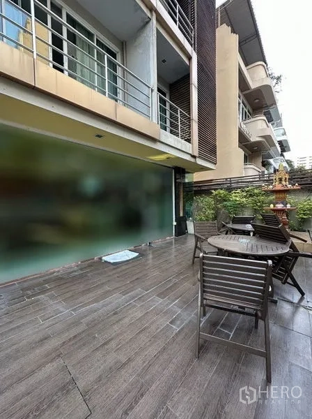 Apartment for rent in Khlong Toei, Bangkok - Ground-floor terrace with outdoor tables, chairs and greenery beside the building.
