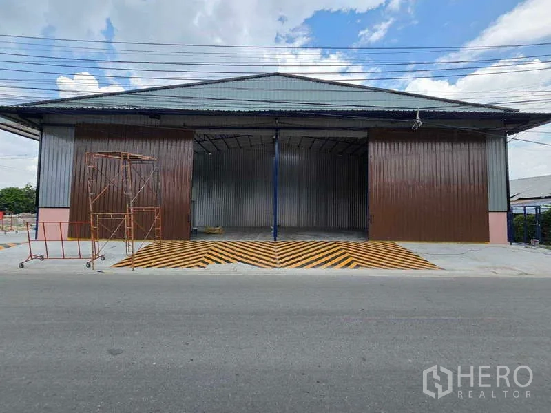 คลังสินค้า ให้เช่าในKhlong Toei, Bangkok - ด้านหน้าโกดังติดถนน ประตูสไลด์เหล็กบานกว้าง พร้อมทางลาดลายเหลืองดำ ในกรุงเทพฯ