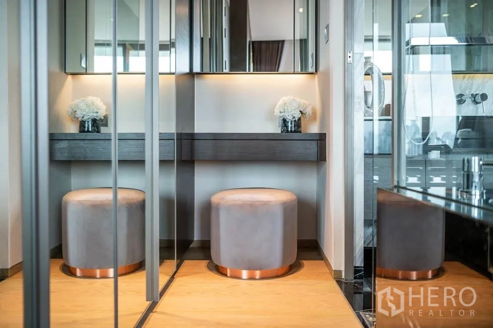 公寓 出租或出售在Bang Rak, Bangkok - 更衣区带镜面衣柜与柔光化妆台，圆形坐墩点缀其间。