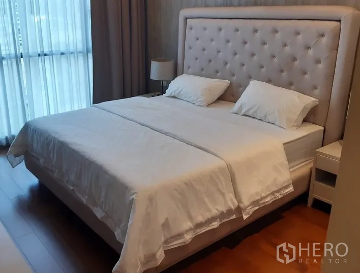 คอนโด ให้เช่าในWatthana, Bangkok - ห้องนอนมาสเตอร์ เตียงคิงไซซ์หัวเตียงบุปุ่ม โคมไฟข้างเตียง และผ้าม่าน