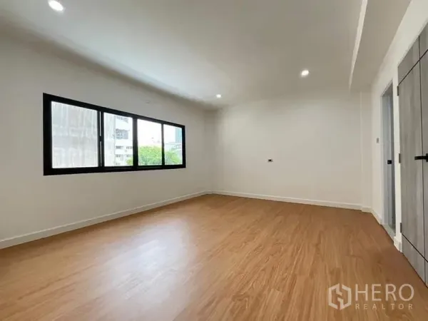 Townhouse for sale in Watthana, Bangkok - Spacious bedroom with wide horizontal window, wood flooring and ceiling spotlights.