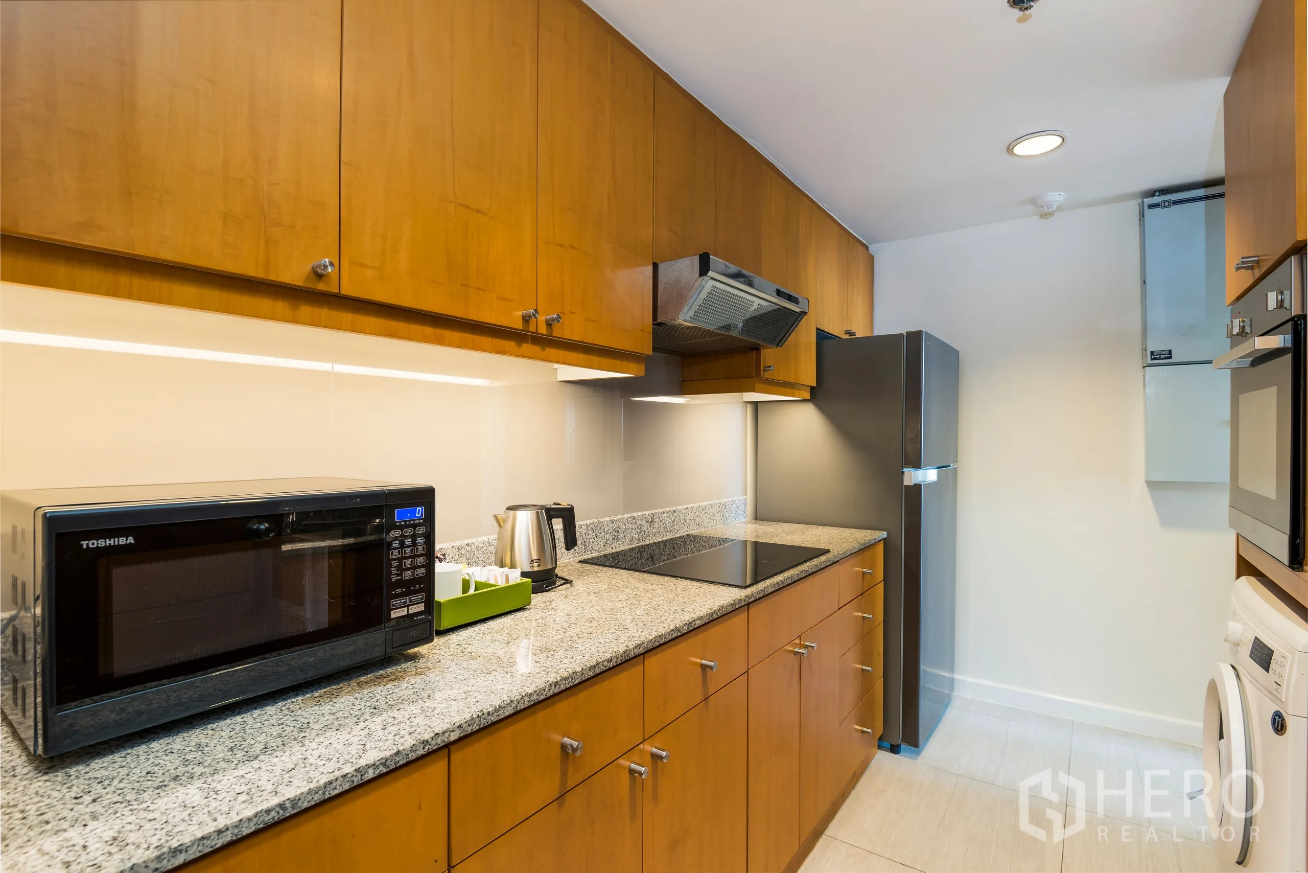 Condominium for rent in Yan Nawa, Bangkok - Modern galley kitchen featuring granite countertops, wooden cabinets, induction hob, microwave and full-size refrigerator.