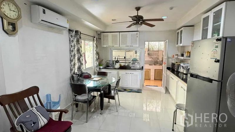Detached House for sale in Mueang Pathum Thani, Pathum Thani - Airy dining area and indoor kitchen with white cabinets, windows and a ceiling fan.