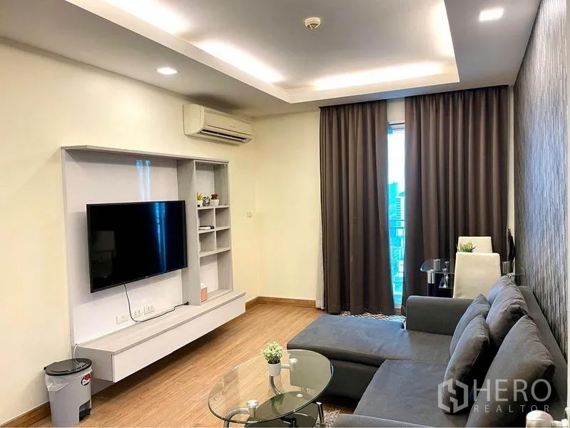 Condominium for rent in Huai Khwang, Bangkok - Modern living room with L-shaped sofa, wall-mounted TV and recessed lighting.