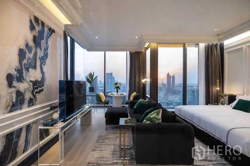 Condominium for rent in Bang Rak, Bangkok - Open studio layout with sofa, TV, dining set and king bed facing a panoramic sunset city view.