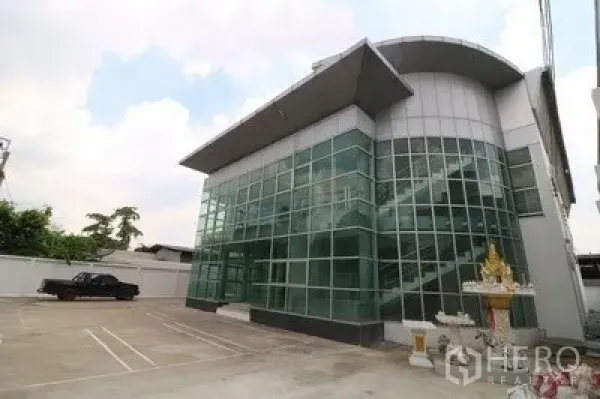 货栈 出租或出售在Prawet, Bangkok - 玻璃幕墙办公楼与仓库外观，前方设宽阔停车区，曼谷Prawet。