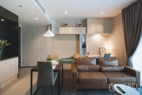 公寓 出租在Watthana, Bangkok - 开放式客餐厅，棕色皮沙发、餐桌与内置书架和书桌。