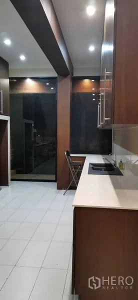 Townhouse for rent in Khlong Toei, Bangkok - Modern galley kitchen with wood cabinetry, white countertops, tiled flooring, and recessed ceiling lights.