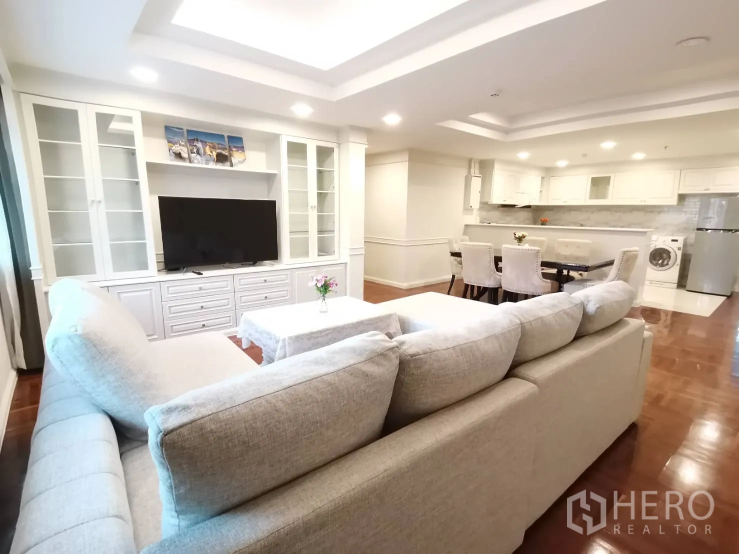 Condominium for rent in Watthana, Bangkok - View from sofa toward dining table, open kitchen with appliances, built-in TV cabinet, and polished wood floor.