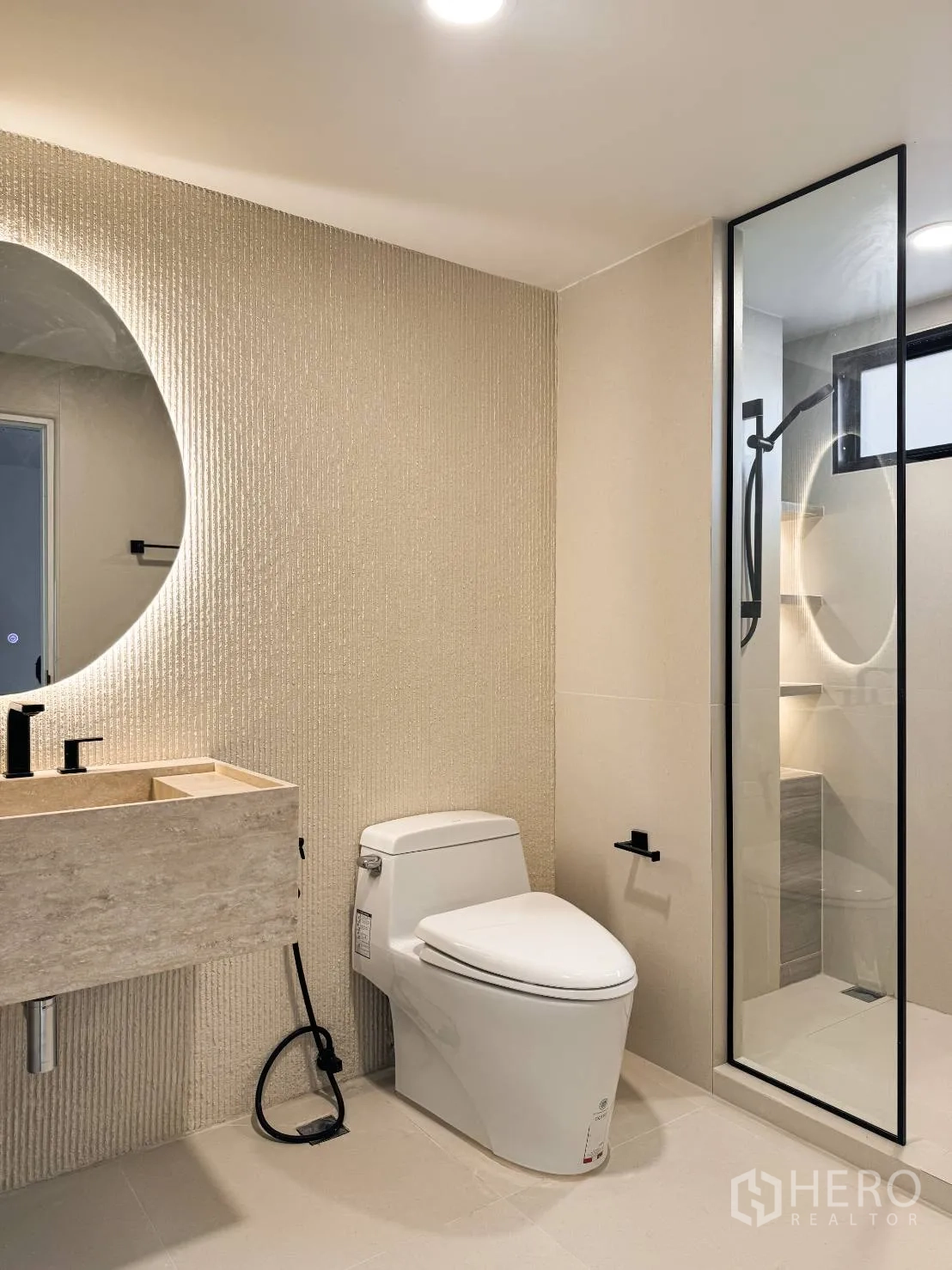 Shophouse for sale in Watthana, Bangkok - Modern bathroom with round backlit mirror, stone vanity, glass shower and toilet.