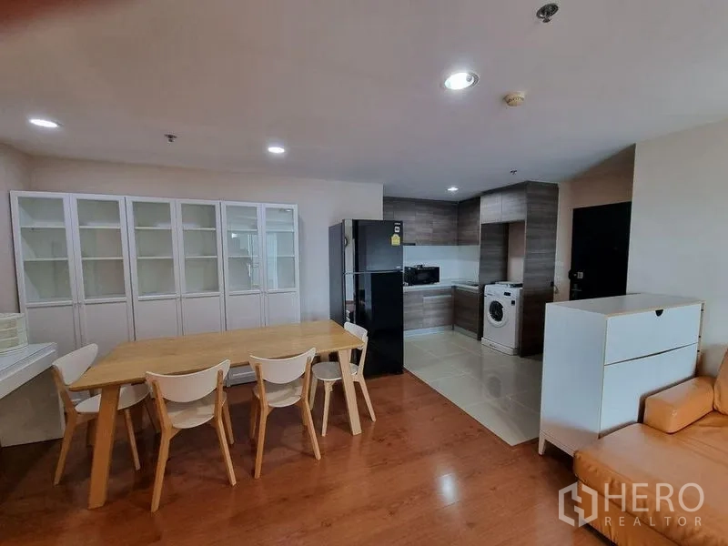 Condominium for rent in Huai Khwang, Bangkok - Four-seat dining table beside glass display cabinets and kitchen with washing machine.