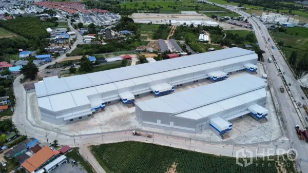 Factory for rent in Bang Lamung, Chon Buri - Aerial view of a modern warehouse and factory complex with multiple loading docks, wide truck yard and surrounding roads and fields.