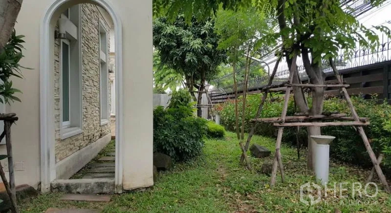 Home Office for rent in Pak Kret, Nonthaburi - Side garden path with archway, mature trees and lawn beside the stone exterior wall.