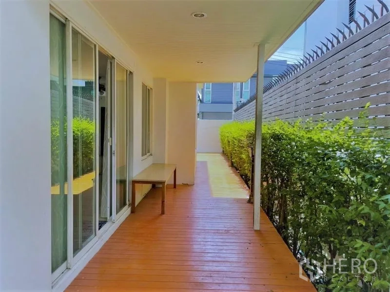 บ้าน ให้เช่าในSuan Luang, Bangkok - ระเบียงไม้ข้างบ้านแบบมีหลังคา ประตูกระจกสไลด์ และแนวพุ่มไม้ให้ความเป็นส่วนตัว.