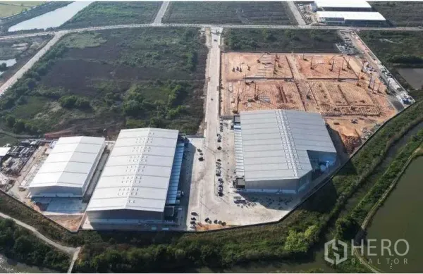 Factory for rent in Bang Bo, Samut Prakan - Drone shot of multiple completed warehouse buildings and new construction plots inside a fenced industrial park bordered by canals and roads.