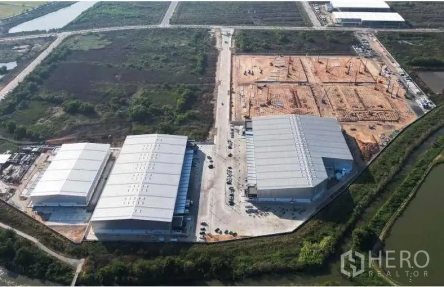 Factory for rent in Bang Bo, Samut Prakan - Drone shot of multiple completed warehouse buildings and new construction plots inside a fenced industrial park bordered by canals and roads.