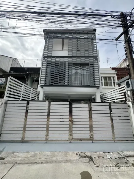 带办公室的家 出租在Phra Khanong, Bangkok - 三层现代家用办公楼外立面，灰色格栅与白色大门。