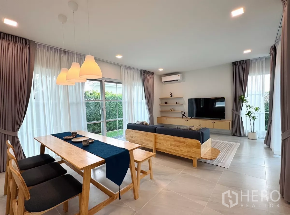 Detached House for rent in Bang Phli, Samut Prakan - Open-plan dining and living room with large windows, sheer curtains and wood furniture.