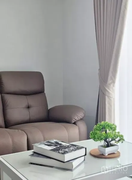 ทาวน์เฮาส์ ให้เช่าในBang Phli, Samut Prakan - มุมพักผ่อนเก้าอี้เอนหลังสีน้ำตาล โต๊ะกลางวางหนังสือ และผ้าม่านยาว.