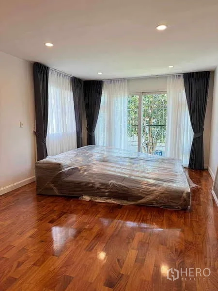 Detached House for rent in Samut Prakan - Corner bedroom with large windows, wood floor, and a bed wrapped for move-in.