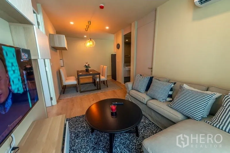 Condominium for rent in Watthana, Bangkok - Cozy living room with sofa and rug facing the dining table in a modern condo.