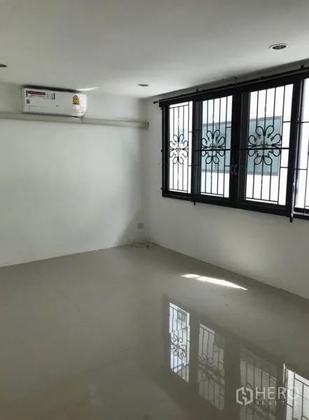 Townhouse for rent in Wang Thonglang, Bangkok - Sunlit bedroom with barred windows, white walls, and wall-mounted air conditioner.