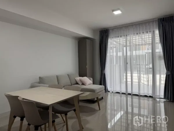 Townhouse for rent in Bang Phli, Samut Prakan - Living room with large sliding glass doors and sheer curtains to the front terrace.