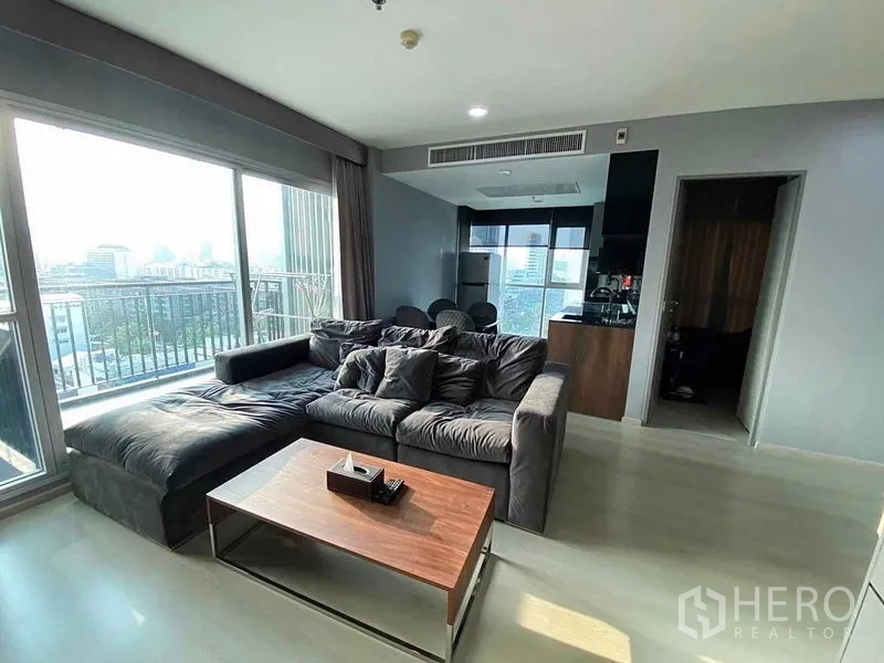 คอนโด ขายในHuai Khwang, Bangkok - มุมนั่งเล่นติดหน้าต่างสูงจรดเพดาน โซฟาตัวแอล และระเบียงชมวิวสกายไลน์