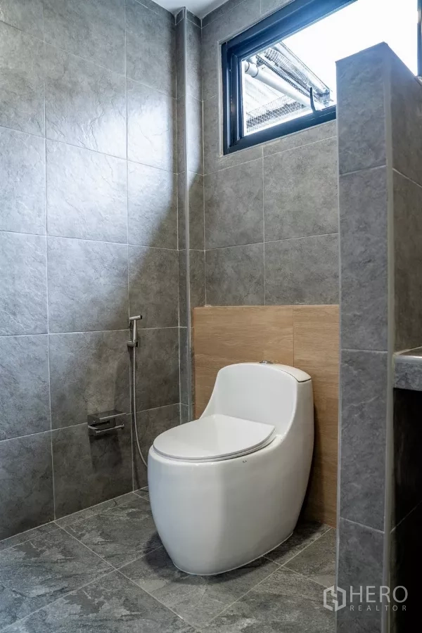 ทาวน์เฮาส์ ขายในWatthana, Bangkok - ห้องน้ำสมัยใหม่ผนังกระเบื้องสีเทา มีหน้าต่างและโถสุขภัณฑ์ชิ้นเดียวพร้อมสายฉีดชำระ