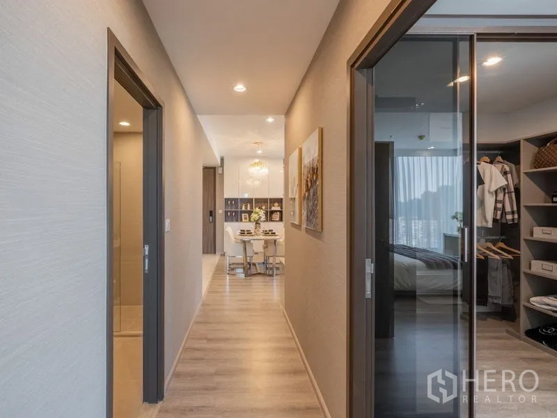 Condominium for rent in Bang Na, Bangkok - Hallway leading to the dining area with artwork on the wall and doors to bedrooms.